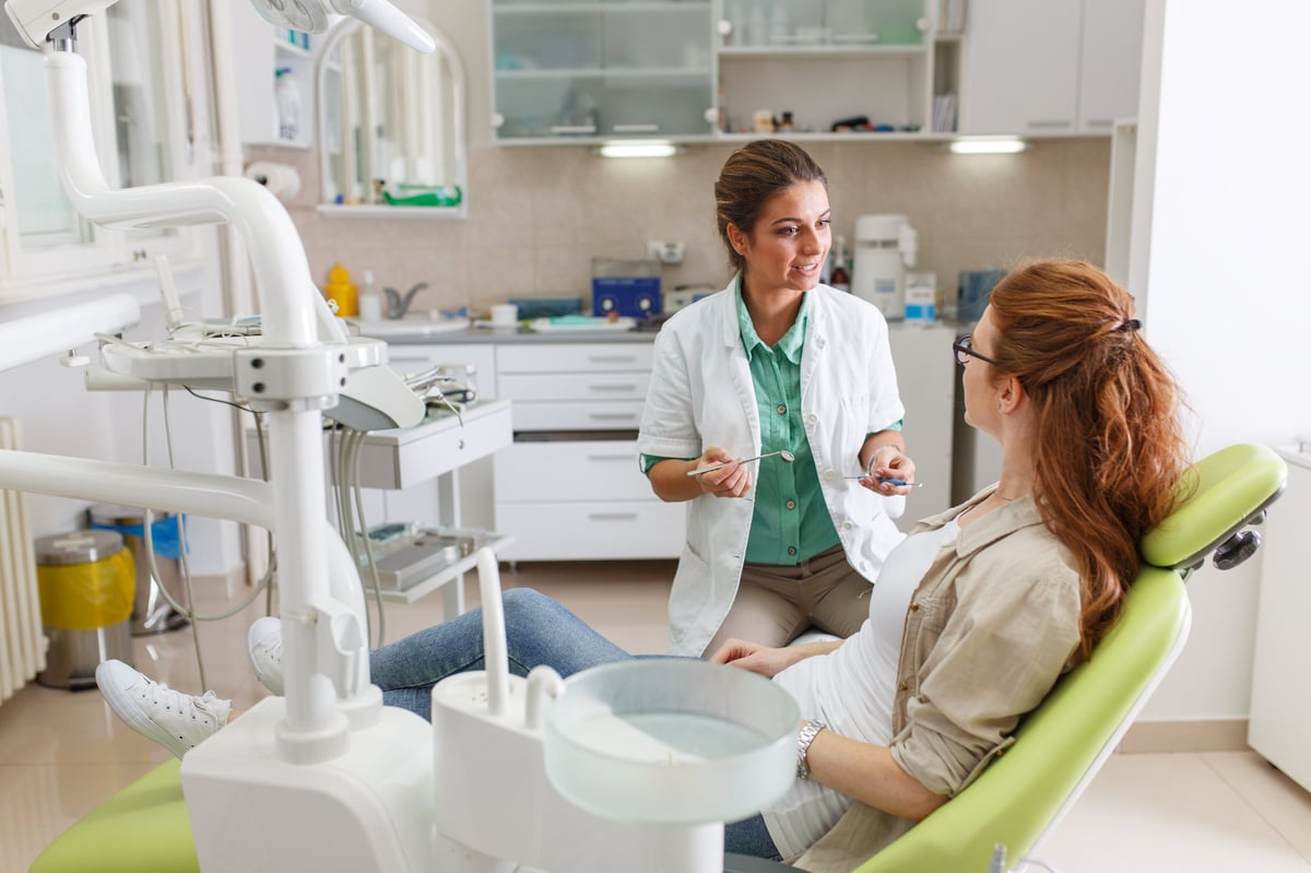 Female dentist in dental office talking with female patient and preparing for treatment.