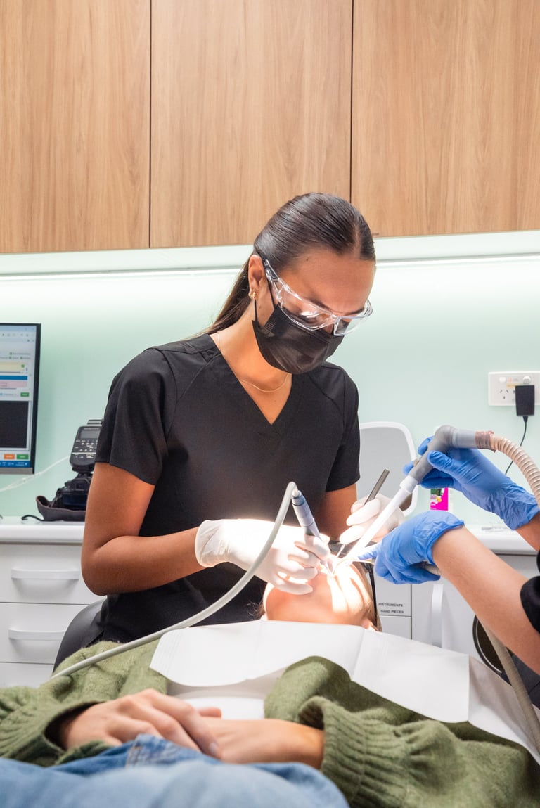 Dental hygienist in black shirt and protective gear examining patients teeth in clinical setting