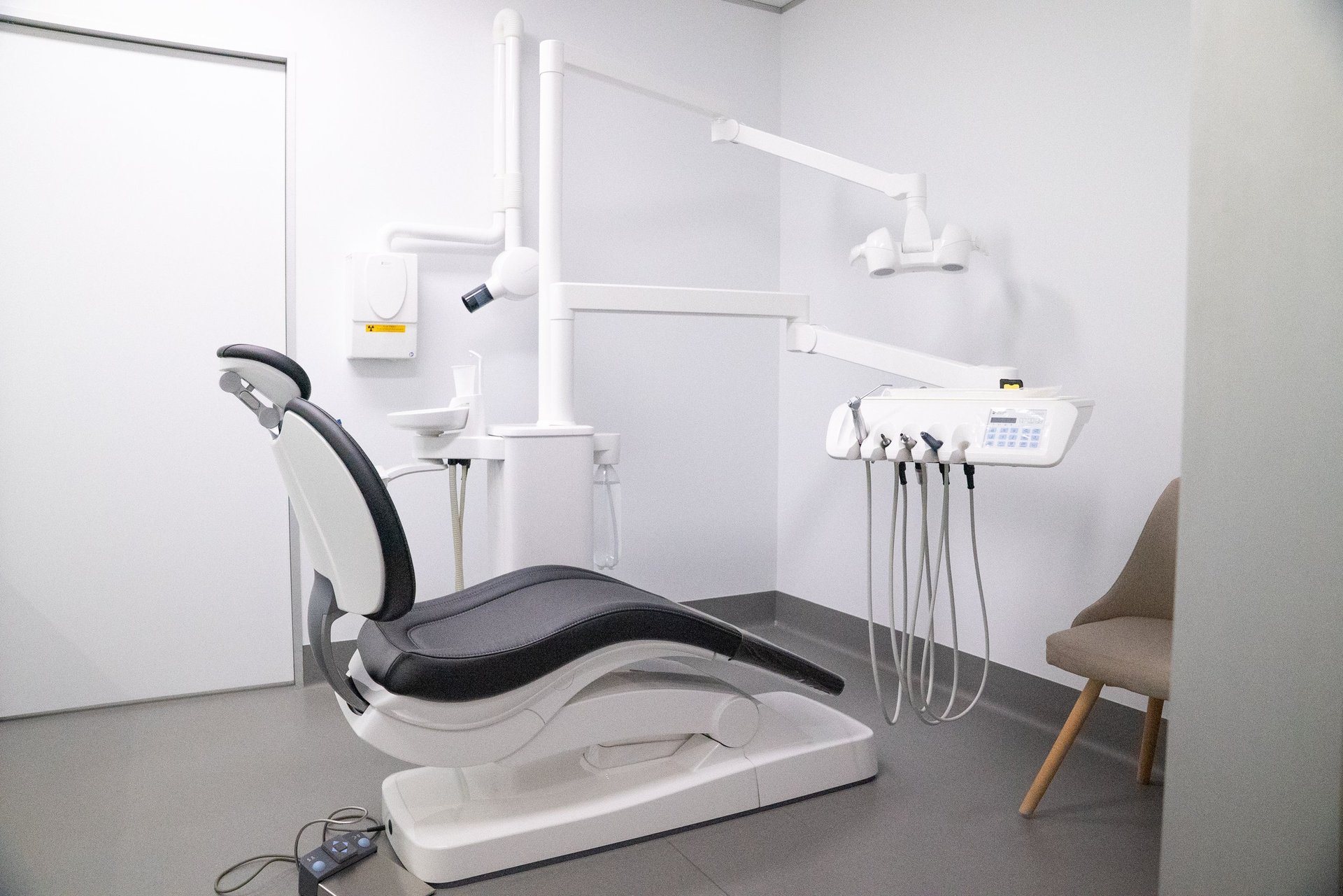 Modern dental treatment room with empty patient chair, overhead light, suction equipment, and control panel against white walls