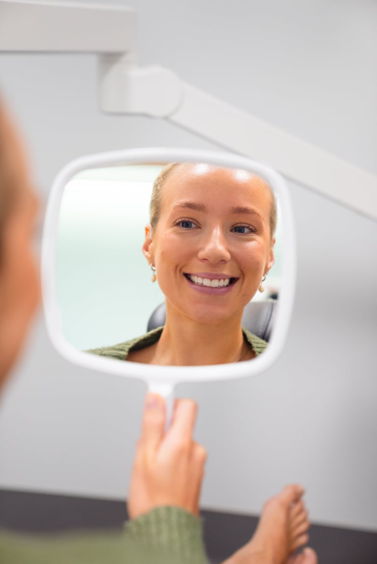 Woman smiling at her reflection in a square mirror during a dental exam