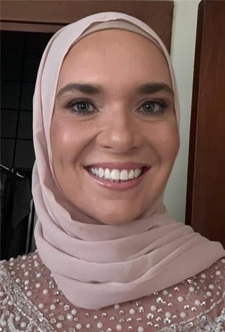 Smiling woman wearing a light pink hijab and beaded top, posing for a close-up portrait indoors
