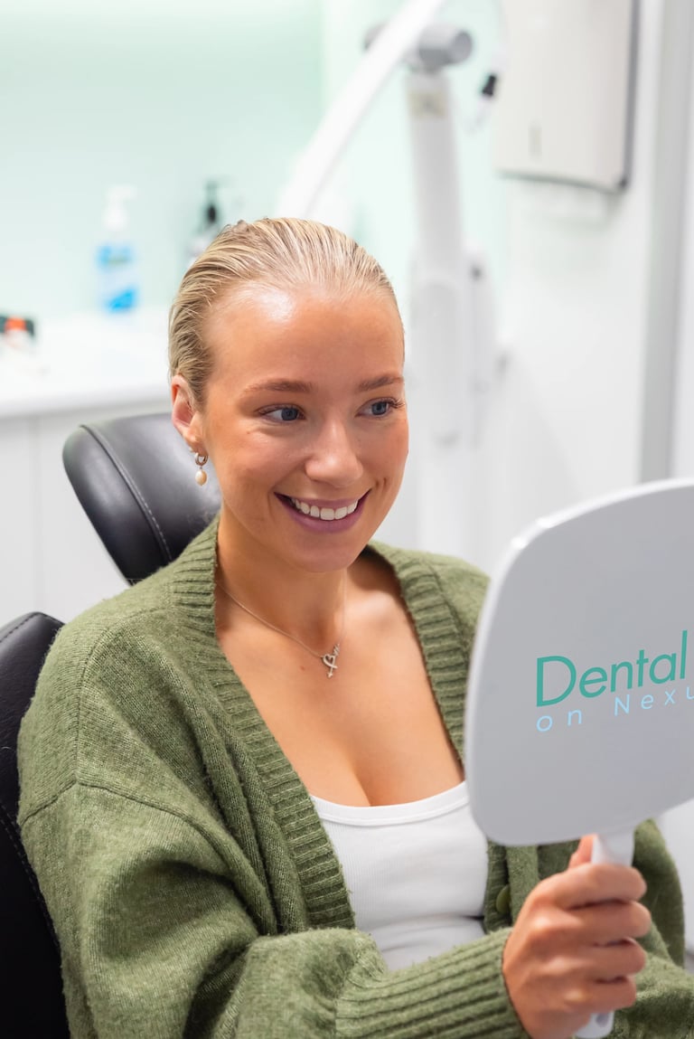 Happy patient holding dental mirror in dental office, wearing green cardigan over white top, sitting in dental chair