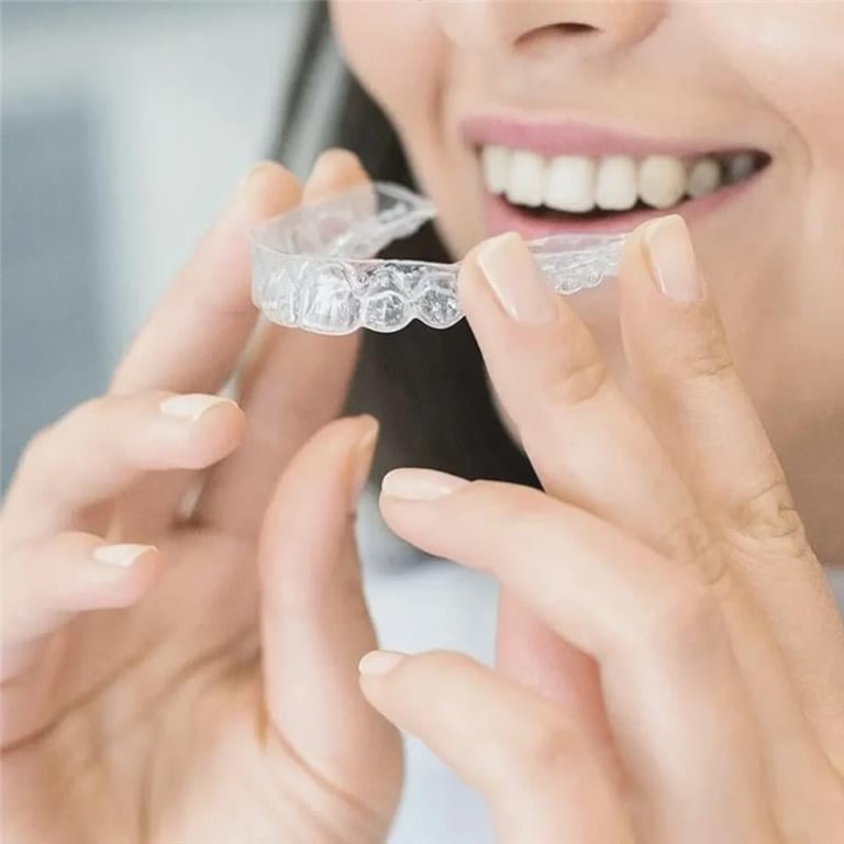 Woman smiling while inserting a clear plastic dental aligner into her mouth for teeth straightening treatment