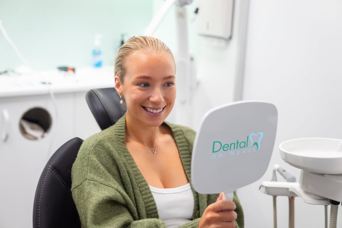 Happy woman smiling while holding a dental mirror in a modern dental office