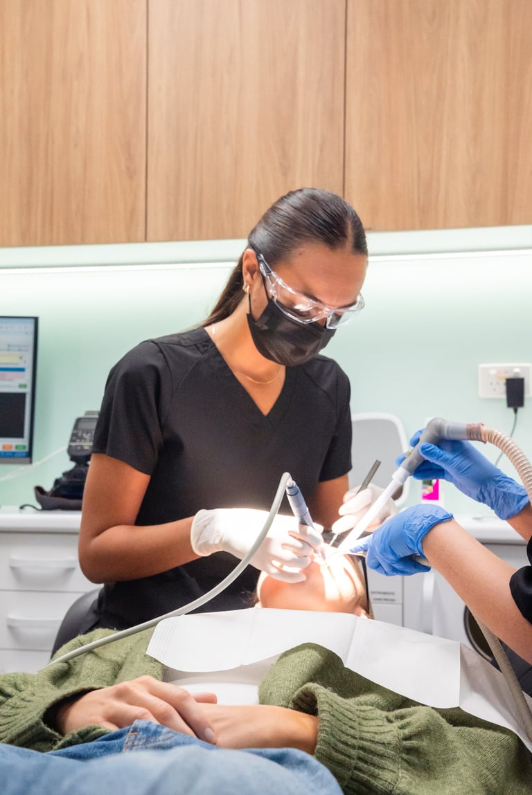 Dental hygienist wearing protective mask and goggles performing teeth cleaning on a patient in a clinic setting
